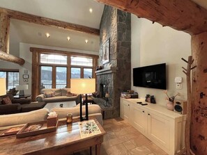 A cozy living room with a stone fireplace, a television, and a large window offering a view.