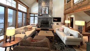 Un salón amplio con chimenea de piedra, vigas de madera y ventanas grandes.