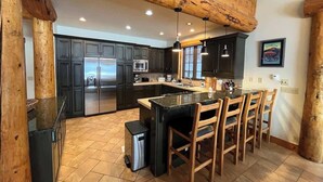 Una cocina con armarios oscuros, una isla central con taburetes de bar, un refrigerador de acero inoxidable y un techo de madera.