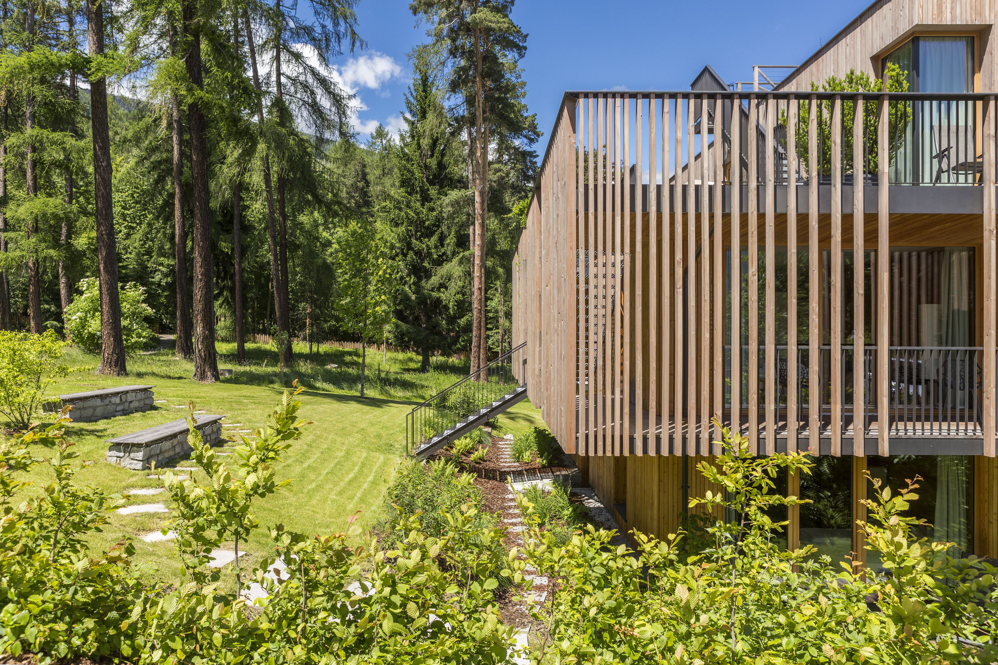 Ein modernes Holzgebäude mit einem Balkon mit Blick auf einen gepflegten Garten und einen bewaldeten Bereich.