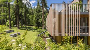 Ein modernes Holzgebäude mit einem Balkon mit Blick auf einen gepflegten Garten und einen bewaldeten Bereich.