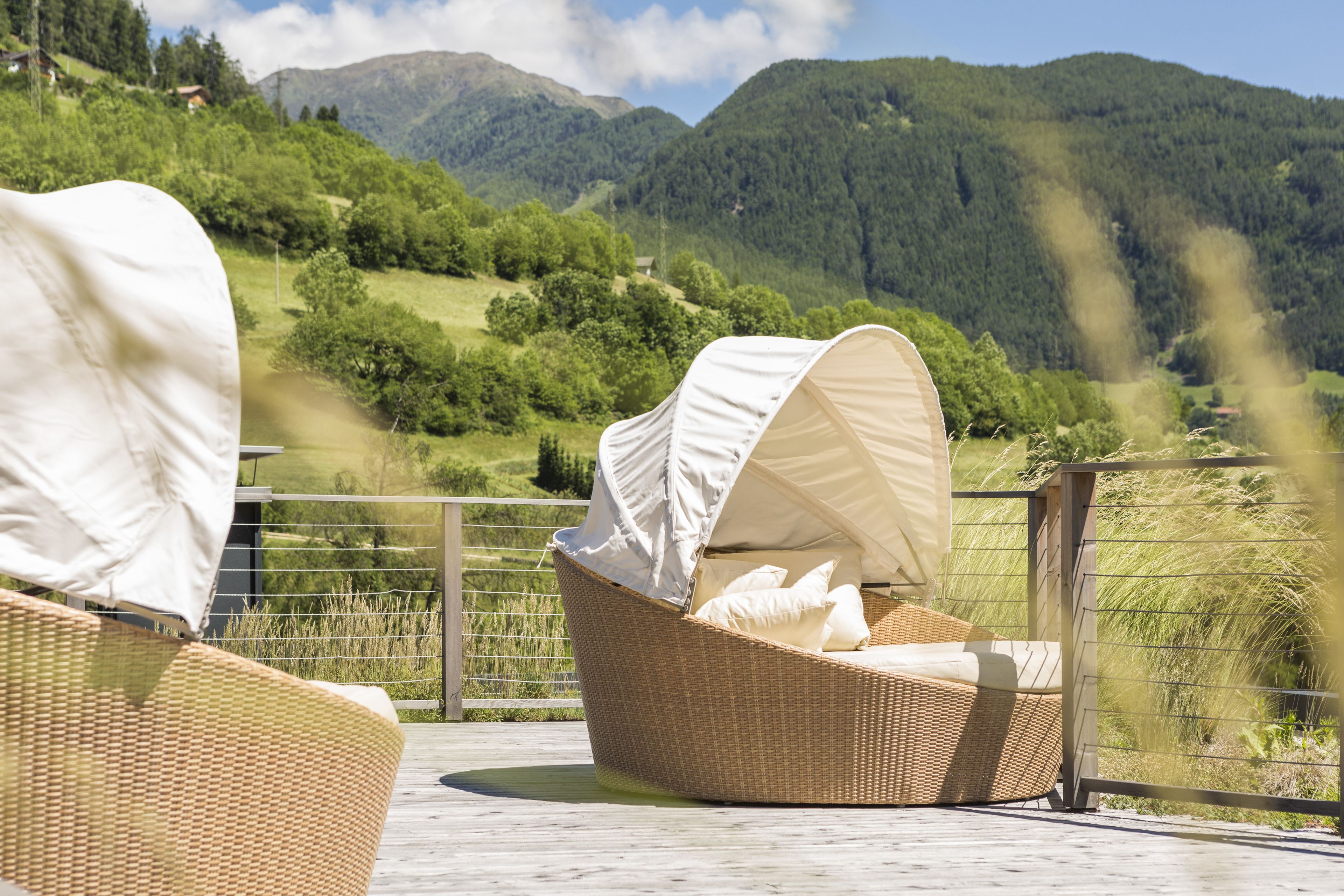 Wicker-Loungemöbel mit weißen Markisen auf einer Terrasse mit Blick auf eine gebirgige Landschaft.