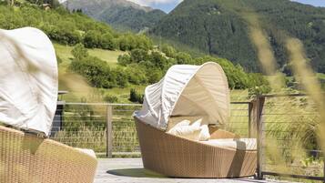 Wicker-Loungemöbel mit weißen Markisen auf einer Terrasse mit Blick auf eine gebirgige Landschaft.