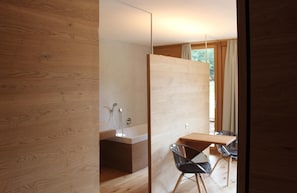 A modern bathroom with a wooden vanity, a shower, and a glass chair.