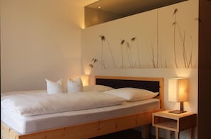 A hotel room with a bed, pillows, a wooden headboard, a nightstand with a lamp, and a wall with a nature-themed mural.