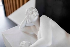 A white sculpture of a reclining figure on a white pedestal.