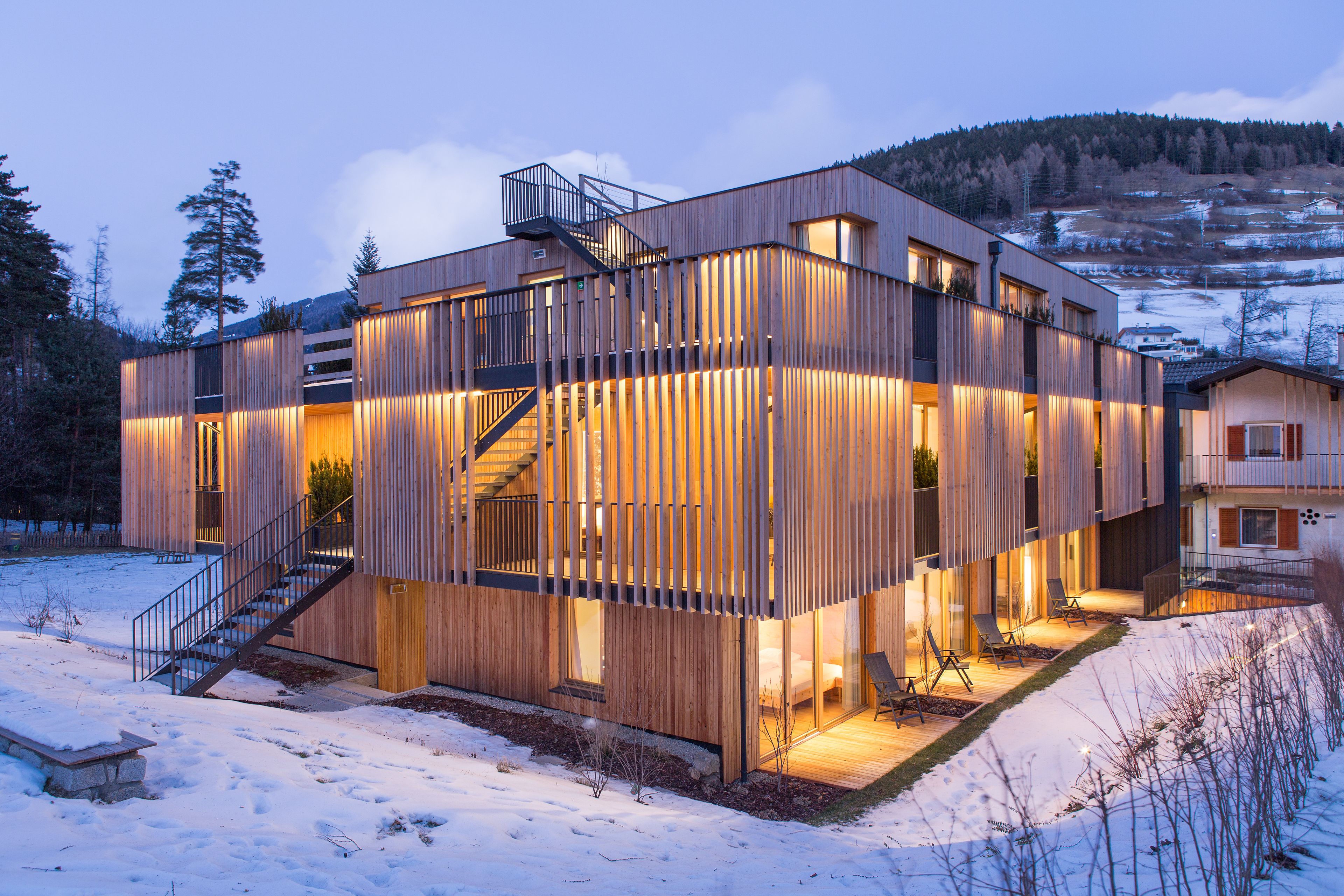 Ein modernes Holzgebäude mit einer Treppe, die zu einem Balkon führt, umgeben von Schnee.