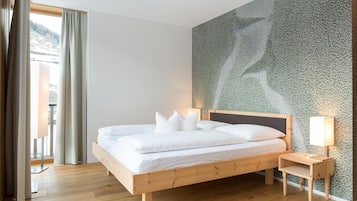 Quarto com cama de madeira, roupa de cama branca, mesa de cabeceira com abajur e parede estampada.
