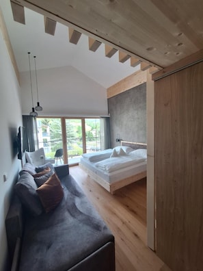 A modern bedroom with a bed, a sofa, and a view of the outdoors.