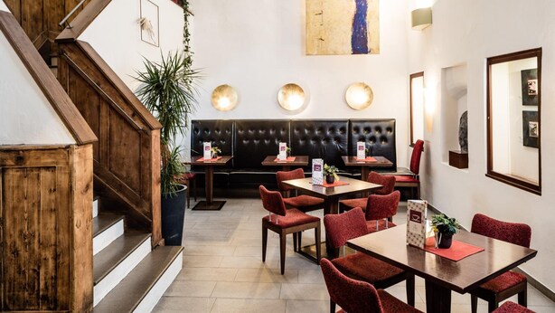 En hotellobby med en trappa i trä, en sittgrupp med röda, klädda stolar och en stor, abstrakt målning på väggen.