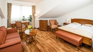 Ett hotellrum med en säng, en soffa, en stol, ett bord med en vas med blommor, en byrå och en lampa.
