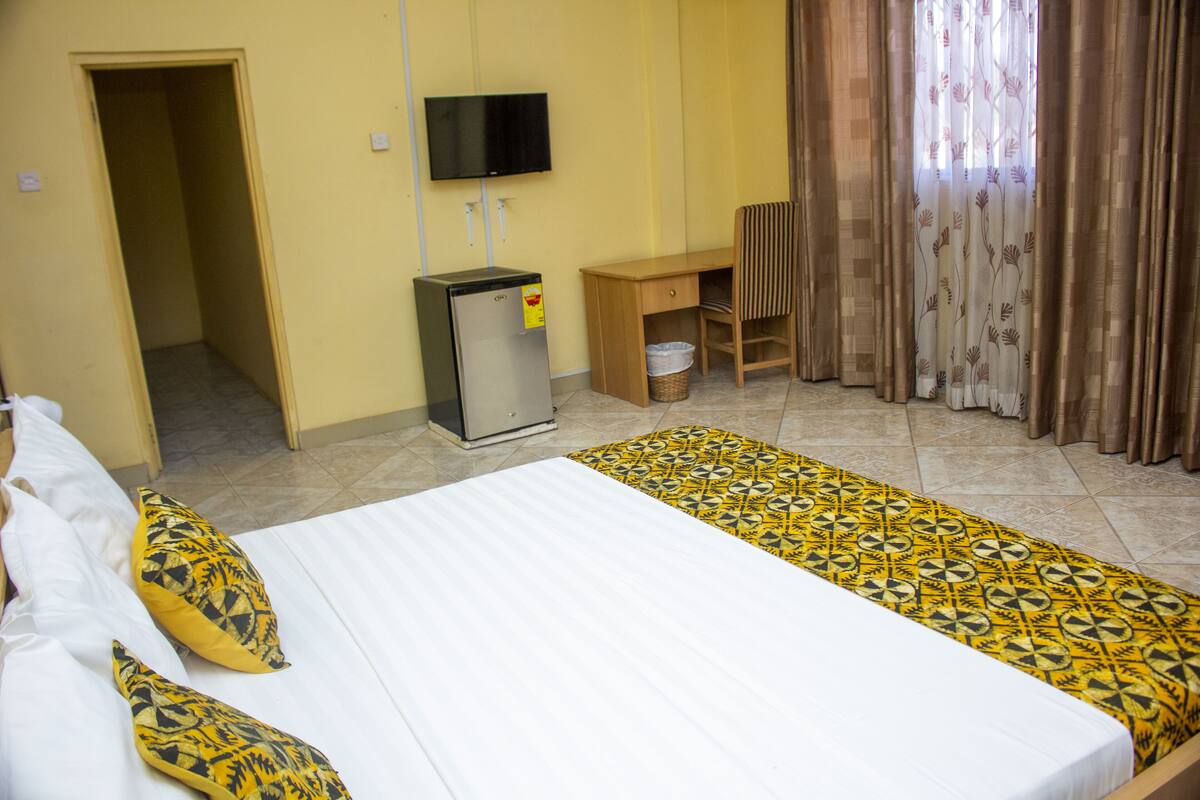 Una habitación de hotel con una cama, un escritorio, un televisor y una ventana con cortinas.