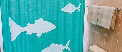 Une salle de bain avec un rideau de douche orné de silhouettes de requins, des toilettes et un porte-serviettes.