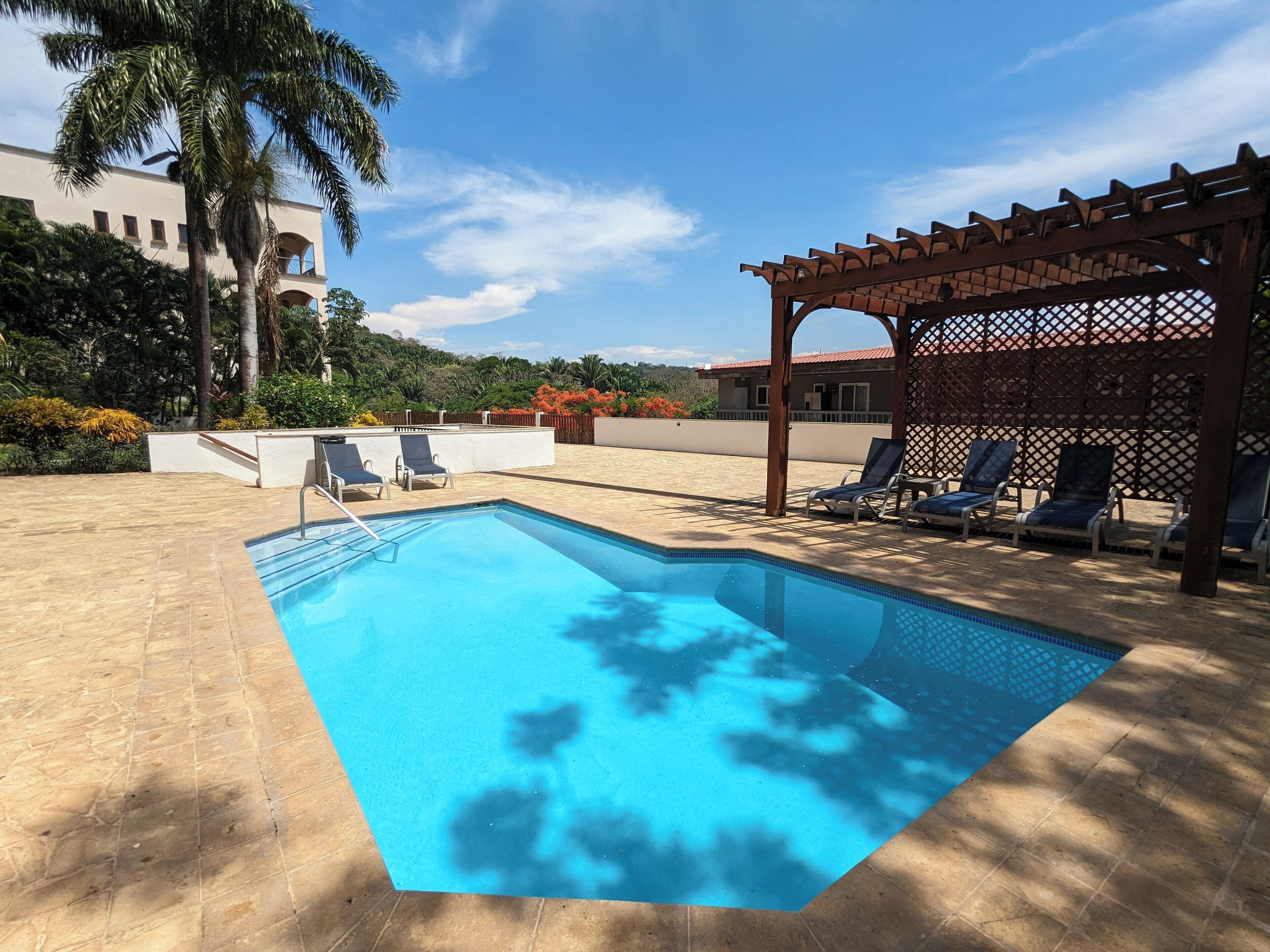 Ein Pool mit Liegestühlen, einer Pergola und einem Gebäude im Hintergrund.