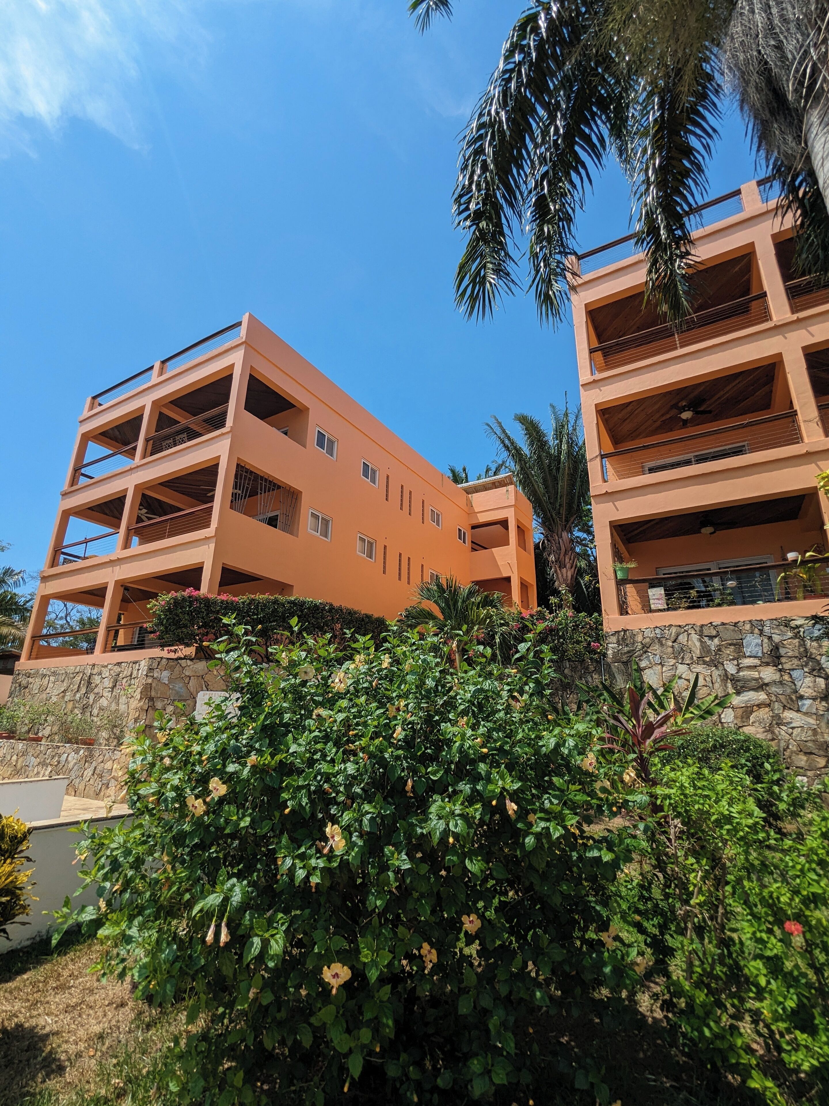 A multi-story building with balconies and a stone wall.