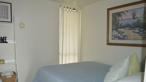 Une chambre à coucher avec un lit, des oreillers, un tableau encadré au mur et une étagère avec des paniers.