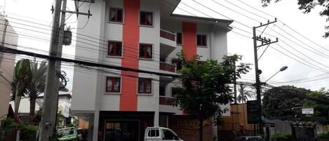 A multi-story building with a red vertical stripe, a white pick-up truck parked in front, and a bicycle with a basket.