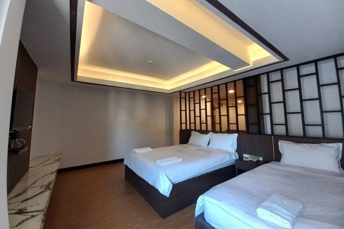 A hotel room with two beds, a modern ceiling design, and a wooden panel wall.
