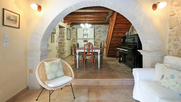 An interior with a dining area under an arched stone ceiling, a piano, and a white sofa. - Villa Pasiphae (Faistos)