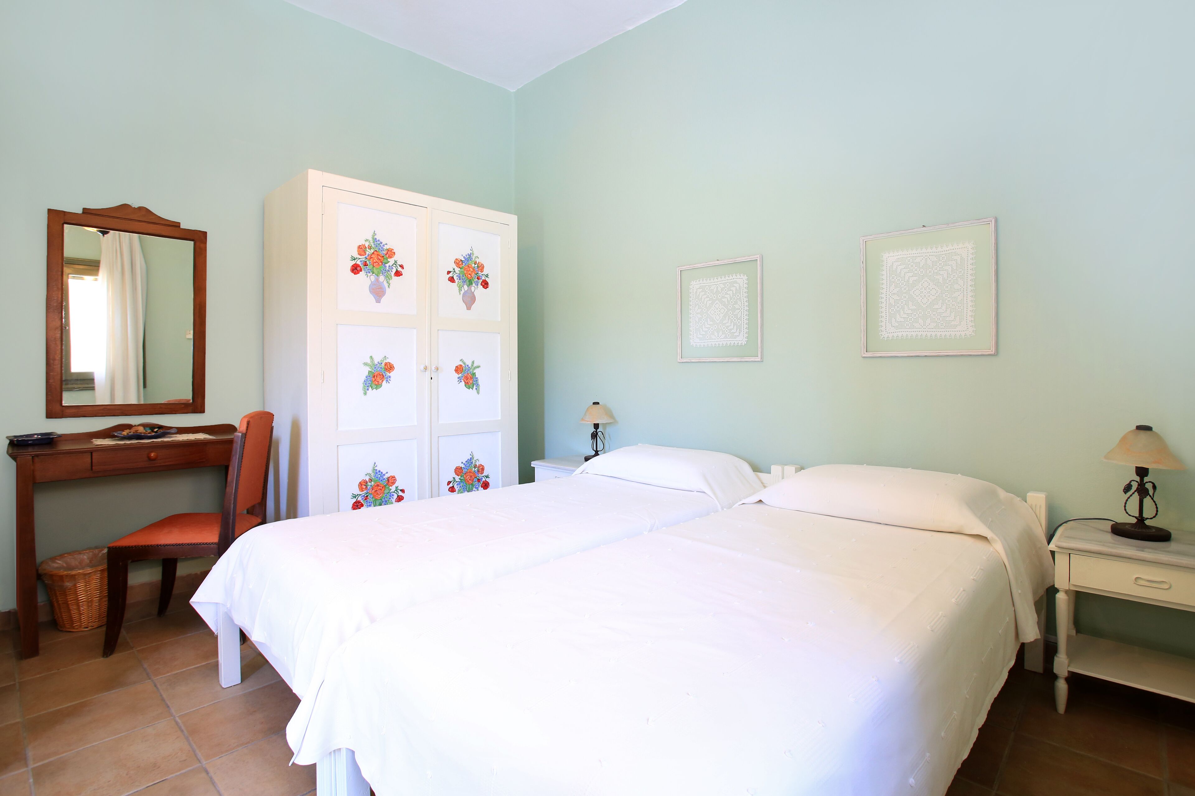 A bedroom with a bed, a desk, a chair, a wardrobe, and two wall-mounted lamps.