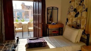 Een kamer met een bed, een bureau met spiegel, een stoel en uitzicht op buiten.