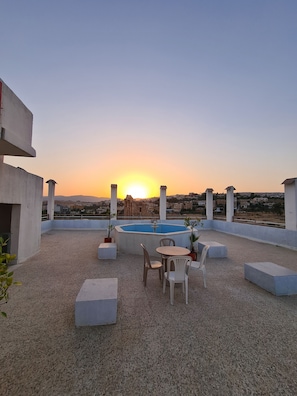 A rooftop terrace with a pool, seating area, and a view of the cityscape at sunset.