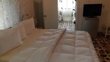 A hotel room with a bed, a television on a stand, and a door leading to a hallway.