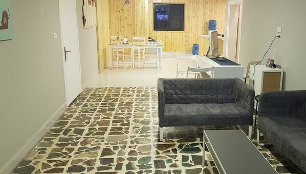 A living room with a stone-patterned floor, two dark sofas, a small table, and a TV in the background.
