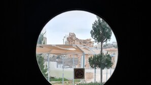 Uitzicht door een rond raam van een gebouw met een stenen gevel, een overdekt terras en een boom.
