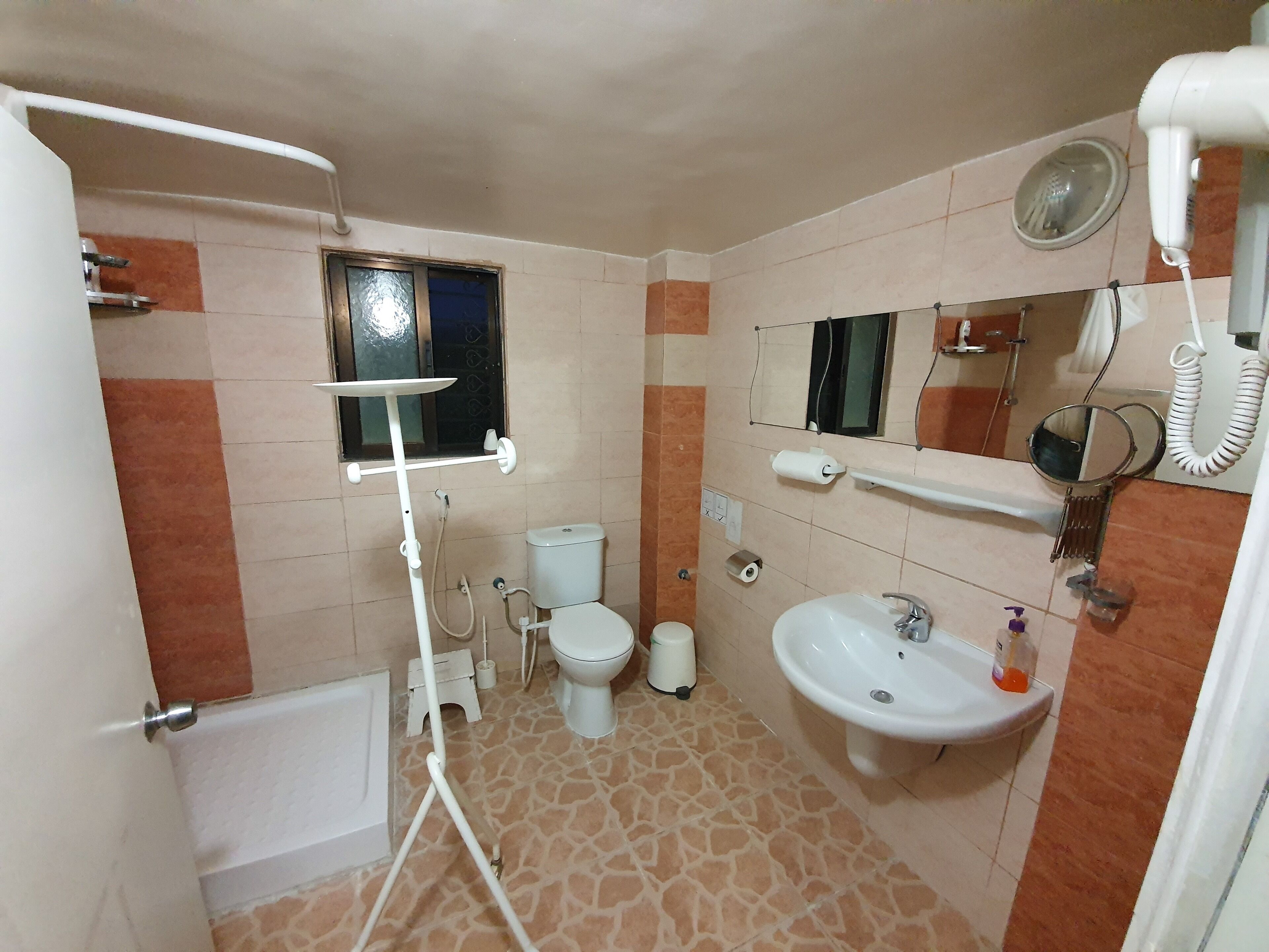 A bathroom with a toilet, sink, mirror, and a window.