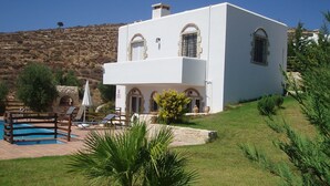 Uma vila branca com piscina, área de estar externa e vista para a colina.