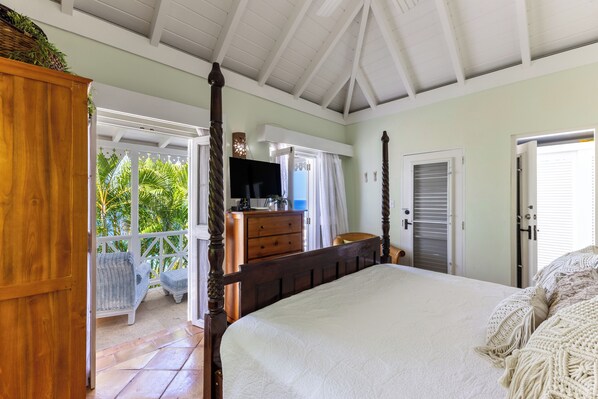 A bedroom with a four-poster bed, a wooden dresser, a television, and a view of the outdoors.