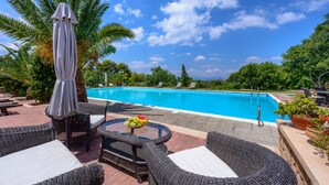 A poolside area with wicker furniture, a table with fruit, and a palm tree. - KOKKINO KASTRO is a historic estate in Aegina full of memories from 1825. (Aegina)