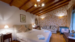 A bedroom with a large bed, a sofa, a stone wall, and a wooden ceiling. - KOKKINO KASTRO is a historic estate in Aegina full of memories from 1825. (Aegina)