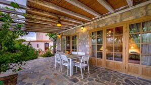 A stone patio with a table and chairs, wooden beams, and a stone building in the background. - KOKKINO KASTRO is a historic estate in Aegina full of memories from 1825. (Aegina)