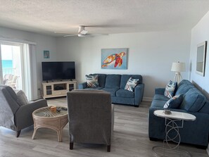 A living room with a TV, two sofas, a chair, a table, and a painting on the wall. - Award Winning Direct Gulf Front Condo with a Fantastic Sunset View (Indian Shores)