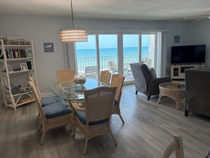 A living room with a glass table, wicker chairs, a grey sofa, a TV, and a view of the sea. - Award Winning Direct Gulf Front Condo with a Fantastic Sunset View (Indian Shores)