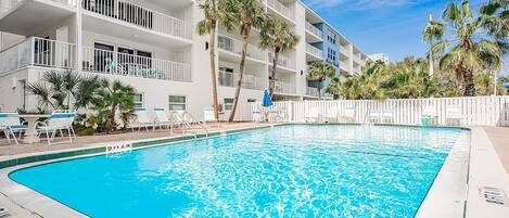 A swimming pool with a white pool deck, surrounded by lounge chairs and palm trees.