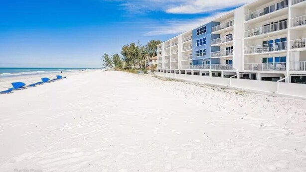 A beachfront hotel with multiple balconies, a sandy beach, and a clear blue sky. - Award Winning Direct Gulf Front Condo with a Fantastic Sunset View (Indian Shores)