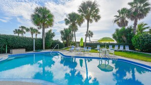 A swimming pool with clear blue water, surrounded by palm trees and lounge chairs.