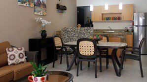 A modern kitchen with a dining area, featuring a tiled backsplash, stainless steel appliances, and a black countertop.