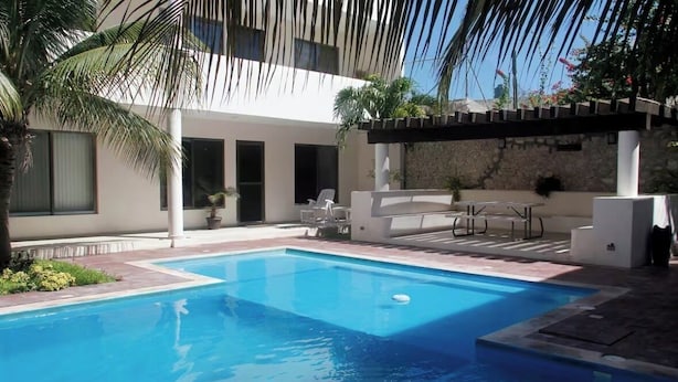 A swimming pool with a pergola, outdoor seating, and a building with large windows and a stone wall.