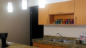 A kitchen with granite countertops, wooden cabinets, a black refrigerator, a sink, and hanging pendant lights.