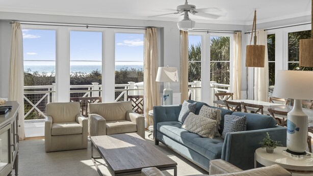 A spacious living room with a large window offering a view of the ocean, a ceiling fan, and a dining area with a table and chairs. - Gulf View Two Story Condo in Watersound | 110B (Panama City Beach)