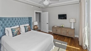A bedroom with a tufted headboard, a bed with white bedding, a wooden dresser, a ceiling fan, and a door leading to another room. - Gulf View Two Story Condo in Watersound | 110B (Panama City Beach)