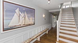 A hallway with a wooden bench, a staircase, and a large framed painting of sailboats. - Gulf View Two Story Condo in Watersound | 110B (Panama City Beach)