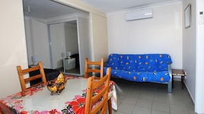 Um quarto pequeno e bem iluminado com uma mesa de jantar, cadeiras, um sofá e um espelho.