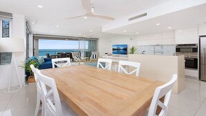 Cozinha moderna com armários brancos, mesa de jantar de madeira e vista para o oceano.