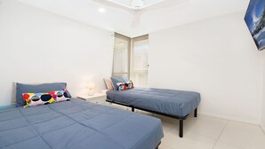 Quarto com duas camas, cada uma com colcha e almofadas azuis combinando, uma mesinha de cabeceira com abajur, e uma janela com vista para uma paisagem nevada.