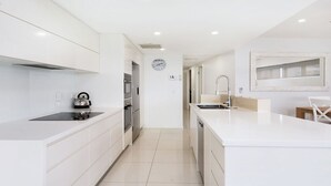 Uma cozinha moderna com armários brancos, uma chaleira sobre a bancada e um relógio na parede.